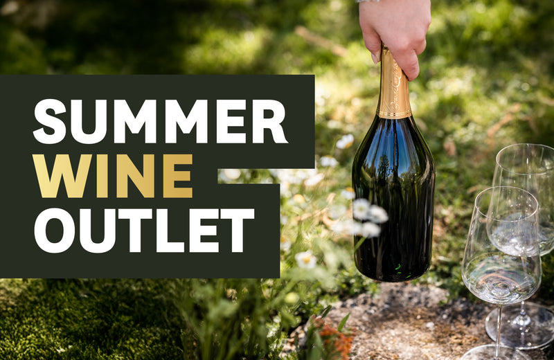 Eine Hand hält eine Weinflasche neben zwei leeren Gläsern im Garten, mit der Aufschrift "Summer Wine Outlet".