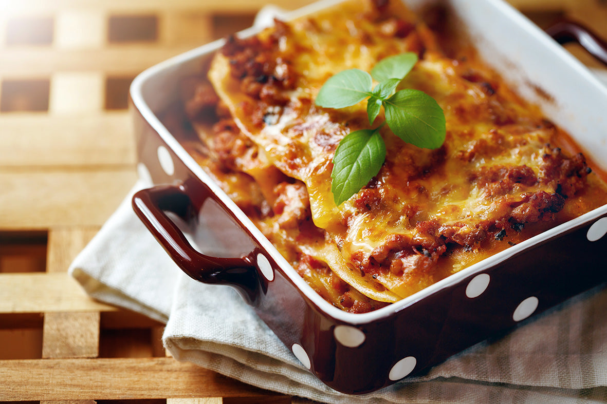 Lasagne in einer rot-weiß gepunkteten Auflaufform, dekoriert mit frischen Basilikumblättern.