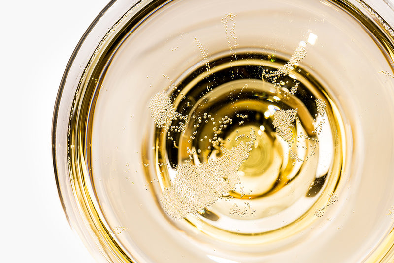 Nahaufnahme eines Glases mit sprudelndem, goldenem Getränk und vielen kleinen Blasen an der Oberfläche.