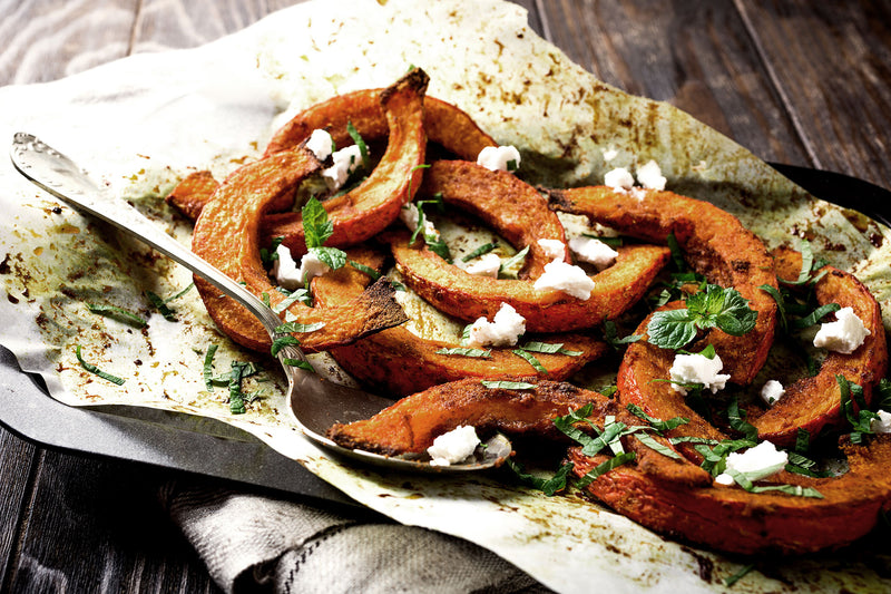 Gebackener Kürbis mit Kräutern und Feta auf einem Backblech mit Löffel.