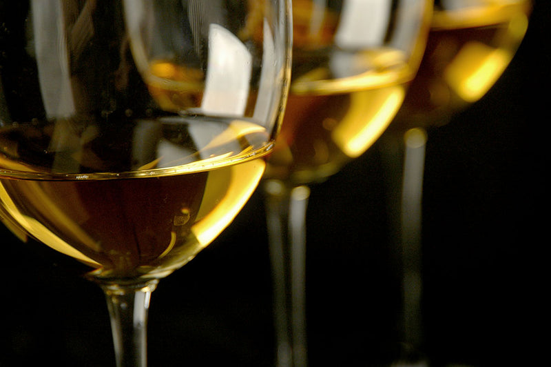Nahaufnahme von drei Weingläsern mit goldenem Weißwein auf schwarzem Hintergrund.