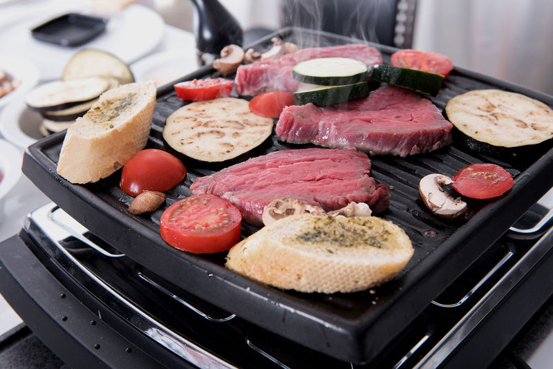 Gemüse, Fleisch, Tomaten und Brot braten auf einem Tischgrill.